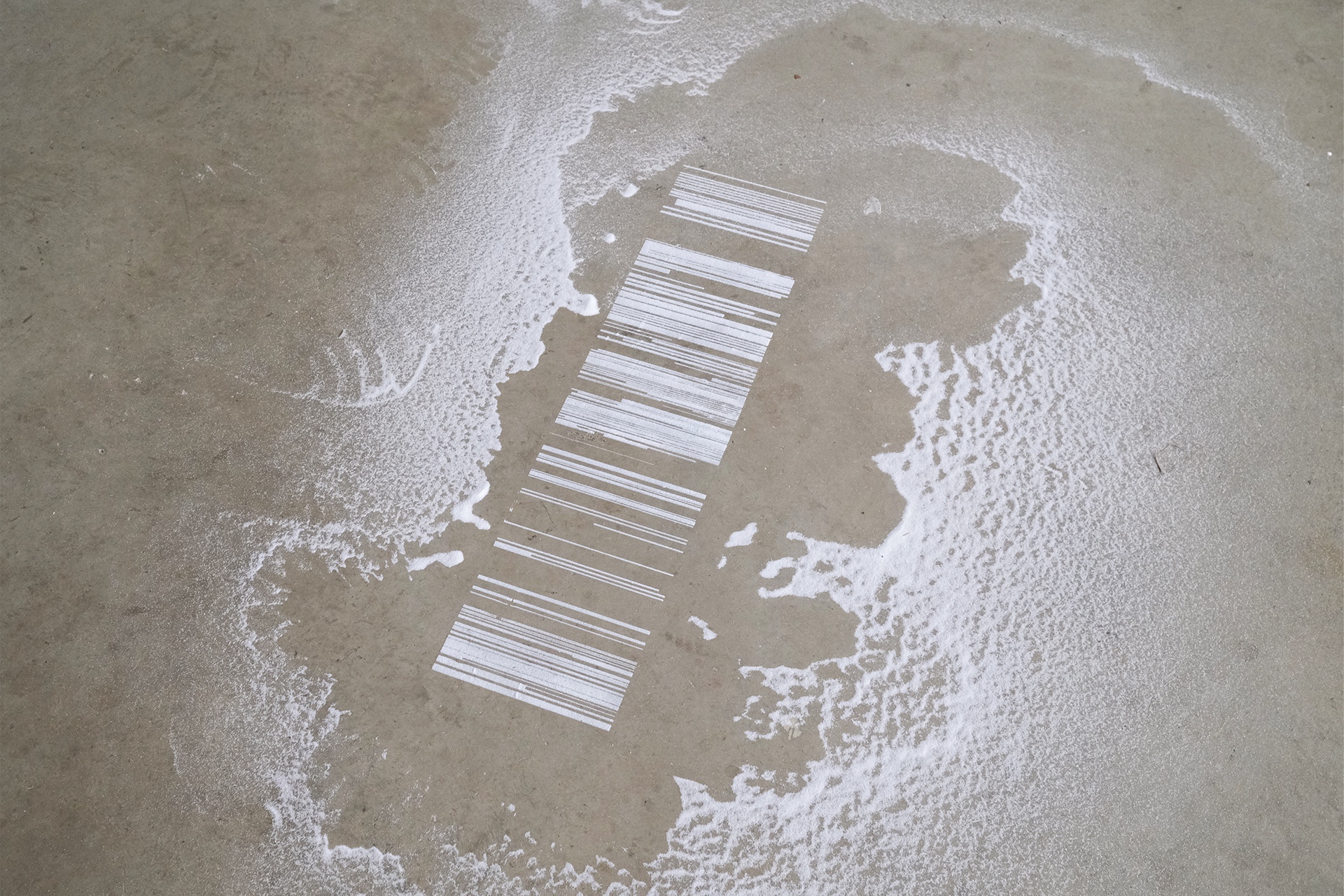 Stripes of varying lengths and thicknesses, running vertically in a long strip to make a perpendicular rectangular shape resembling satellite imagery of salt evaporation ponds. Each stripe is made purely from granular salt and contrasts significantly again