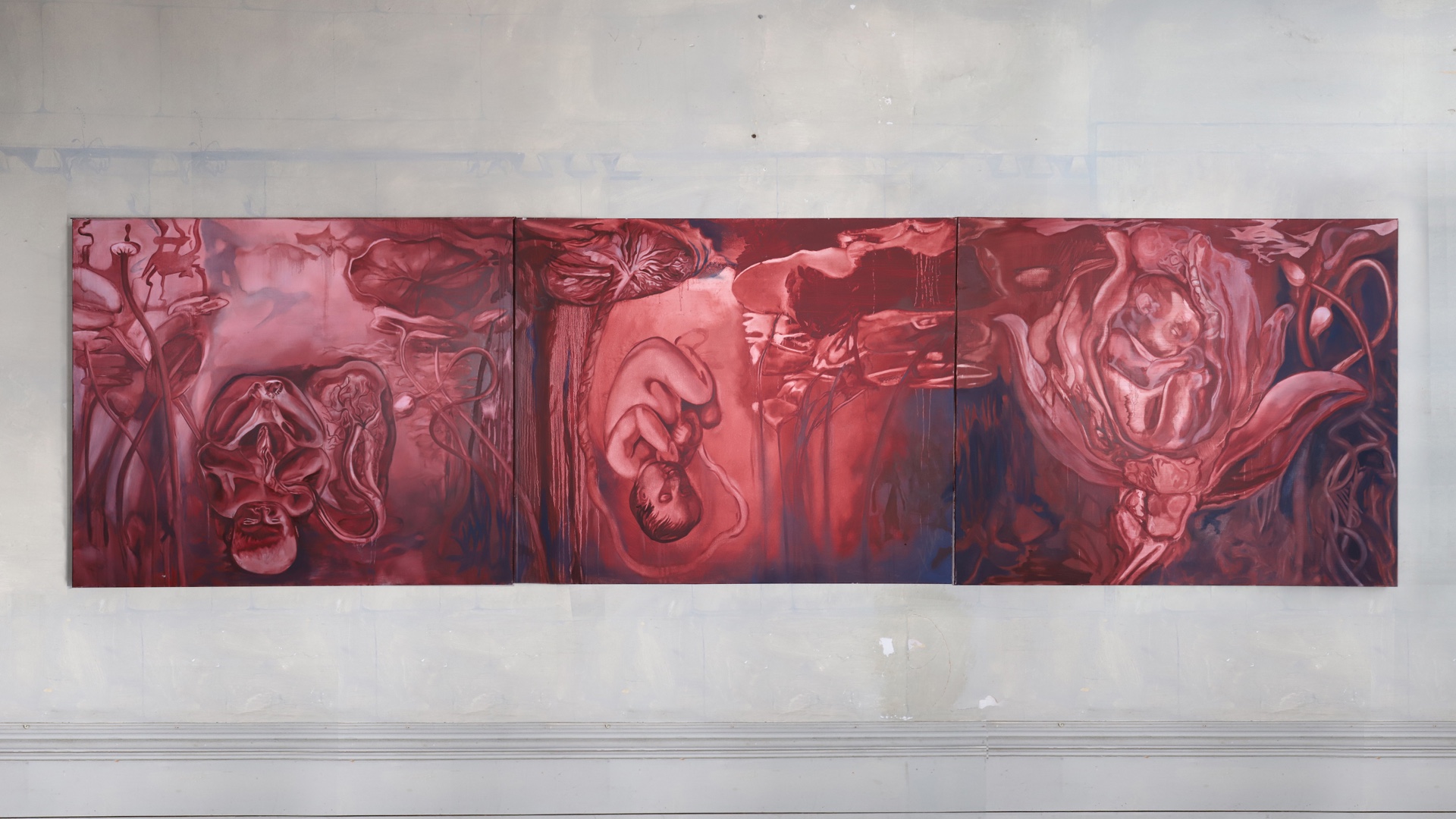 A triptych red monochrome painting of three foetus' submerged under a pond, with dark blue shadows.