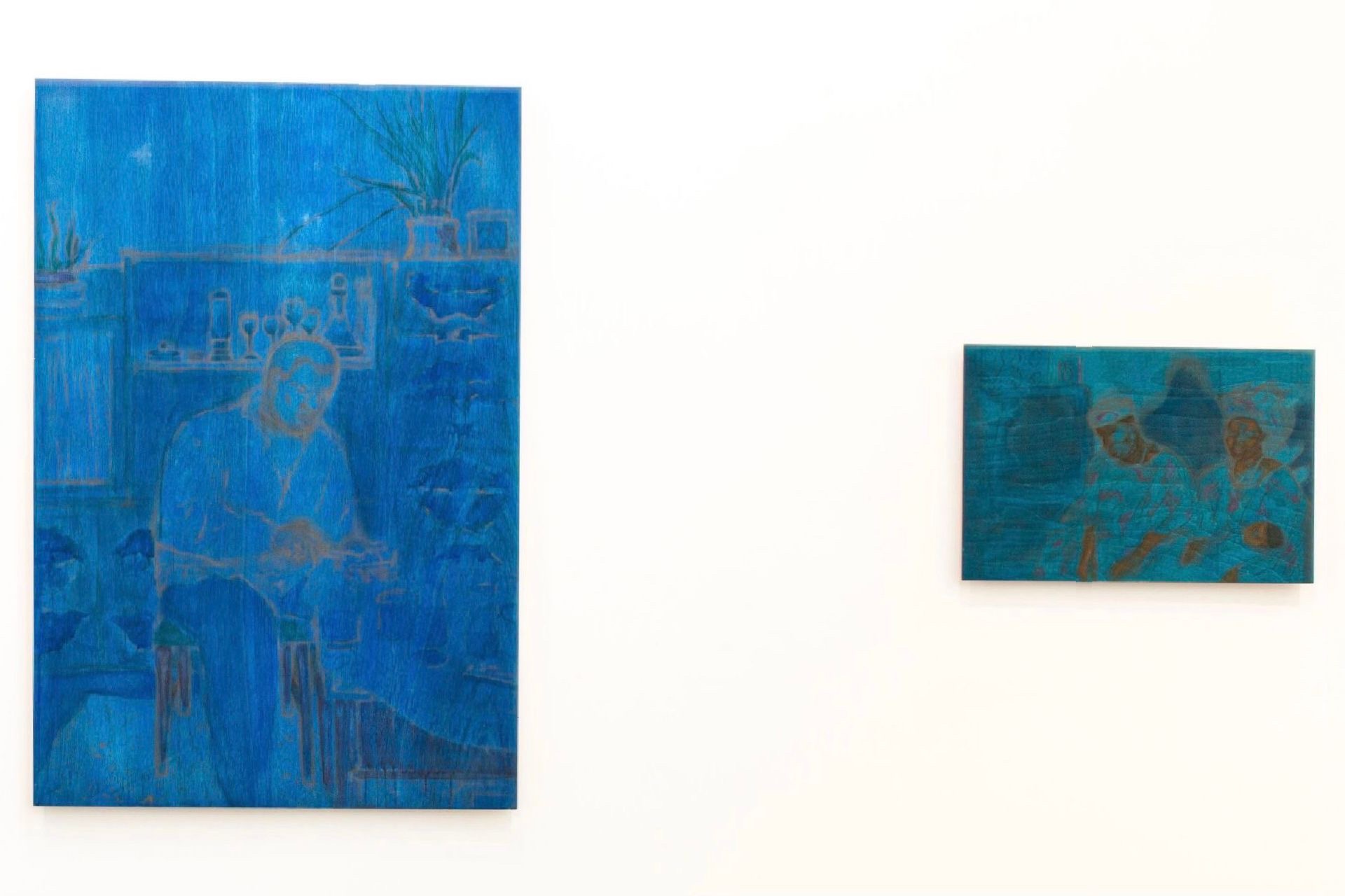 An installation shot of two works, on the left is a larger scale painting on wood. The figure is located in a blue hued domestic space, he seems to be holding a table knife and a slice of bread. 