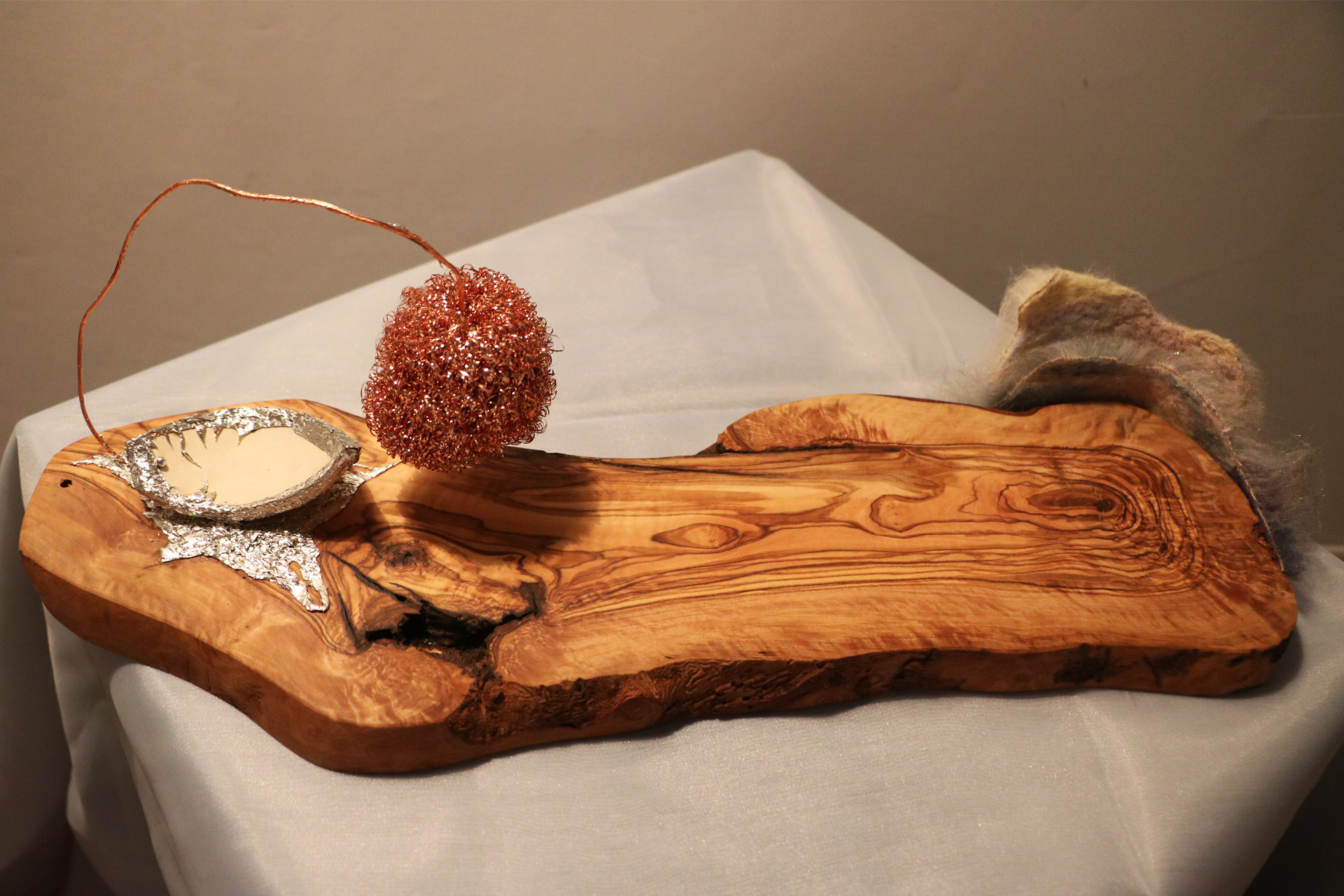 At the bottom is a wooden board with a grain pattern resembling flowing water. In the upper left corner of the board lies a ceramic piece shaped like a small boat, encased in tin. Above the ceramic extends a copper wire connected to a copper wire ball rese