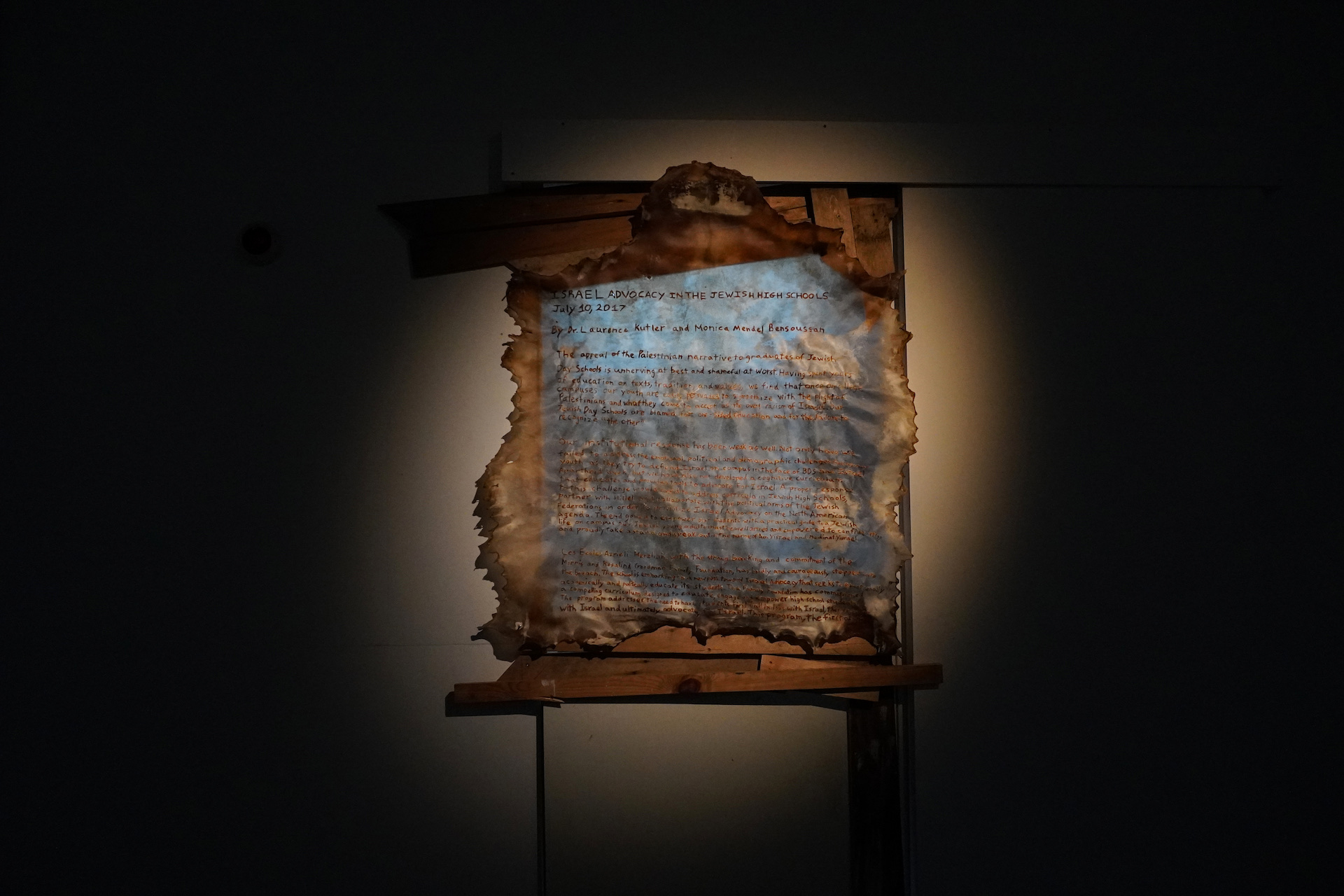 A large sheet of rawhide goatskin, with handwriting etched into it by heat - lit by spotlight.