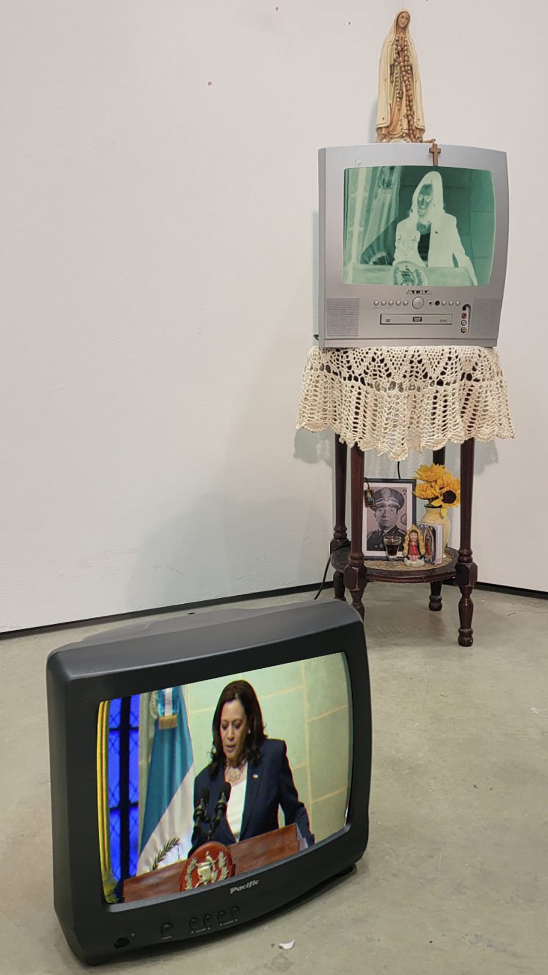 2 CRT TVs against white panels. A looped video of Kamala Harris in Guatemala plays on both TVs