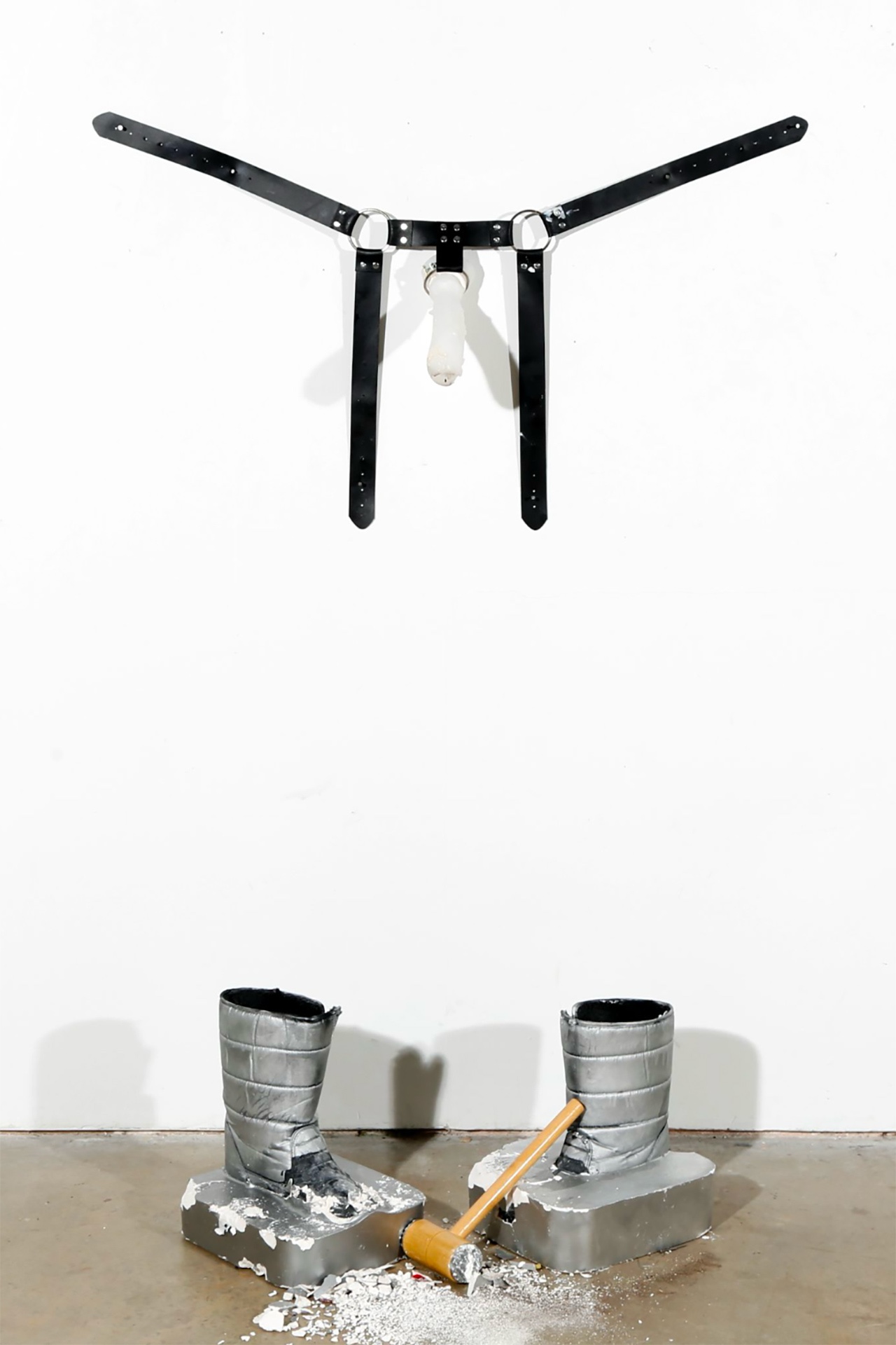 Strap on wall with crushed boots on floor- mountaineer boots, faux leather chest brace, metal ring, nails, tenderiser
