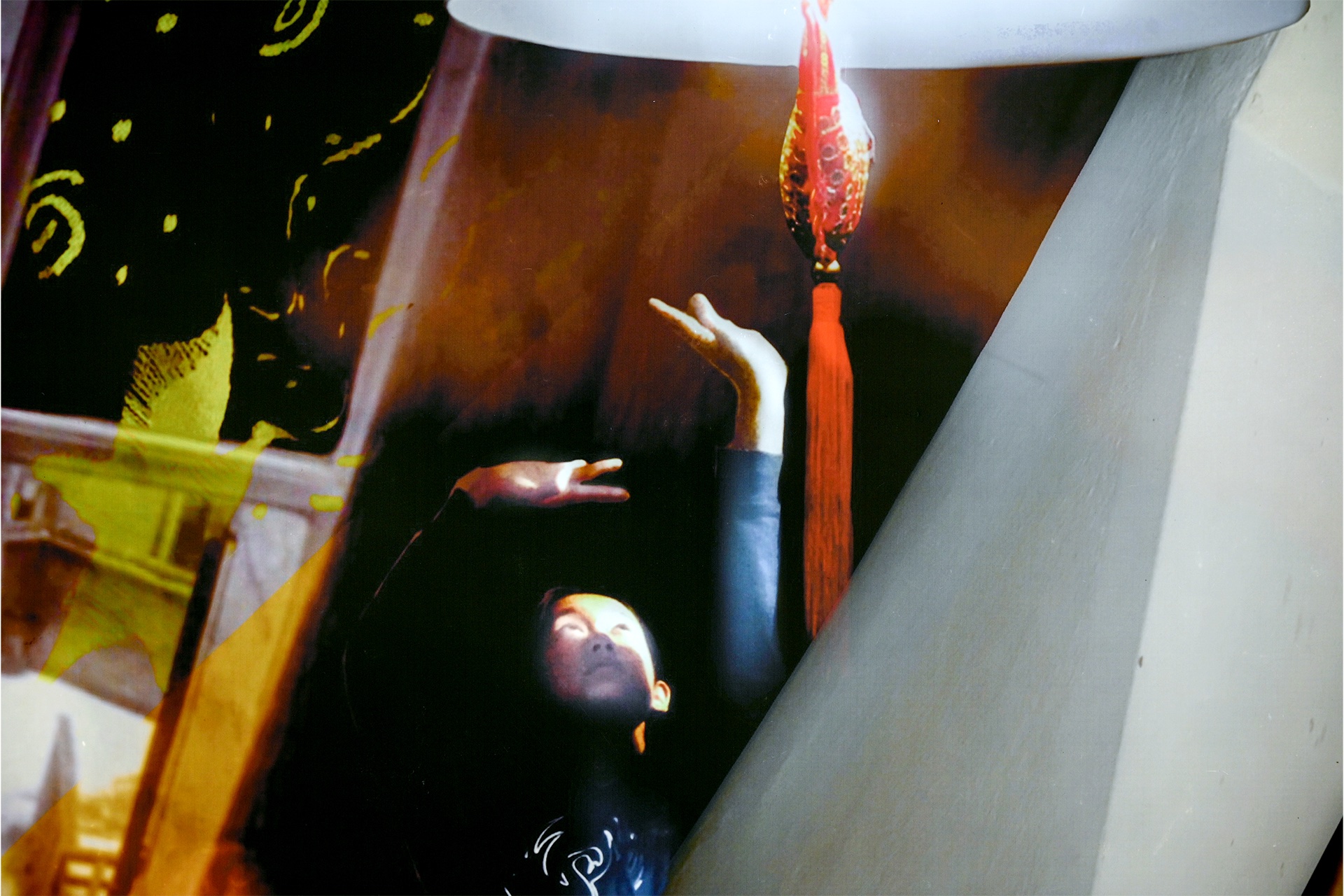 A person reaching towards a red ornament hung from a ceiling lamp.