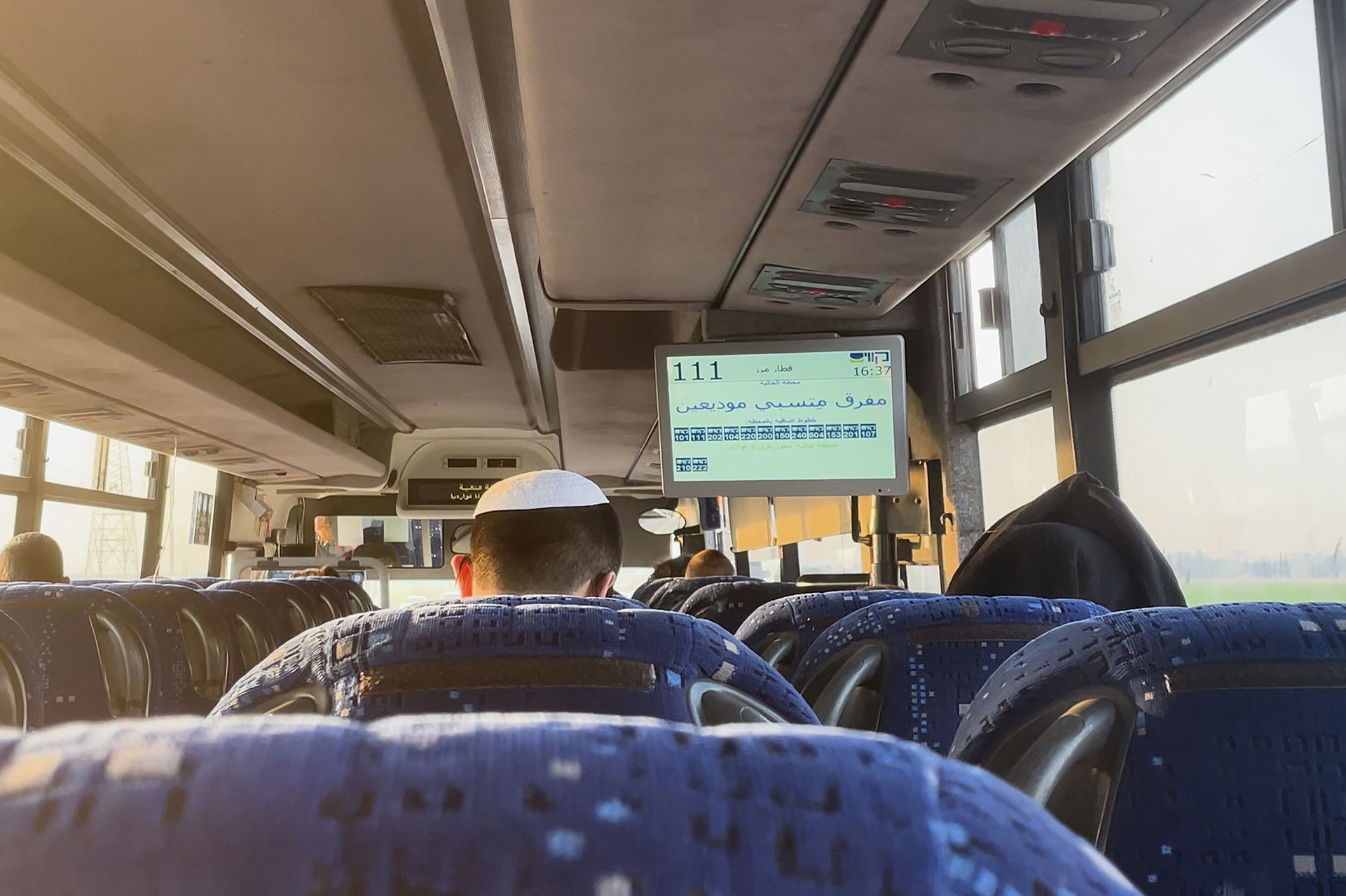 View from the back of a bus, featuring headrests and men wearing kippot.
