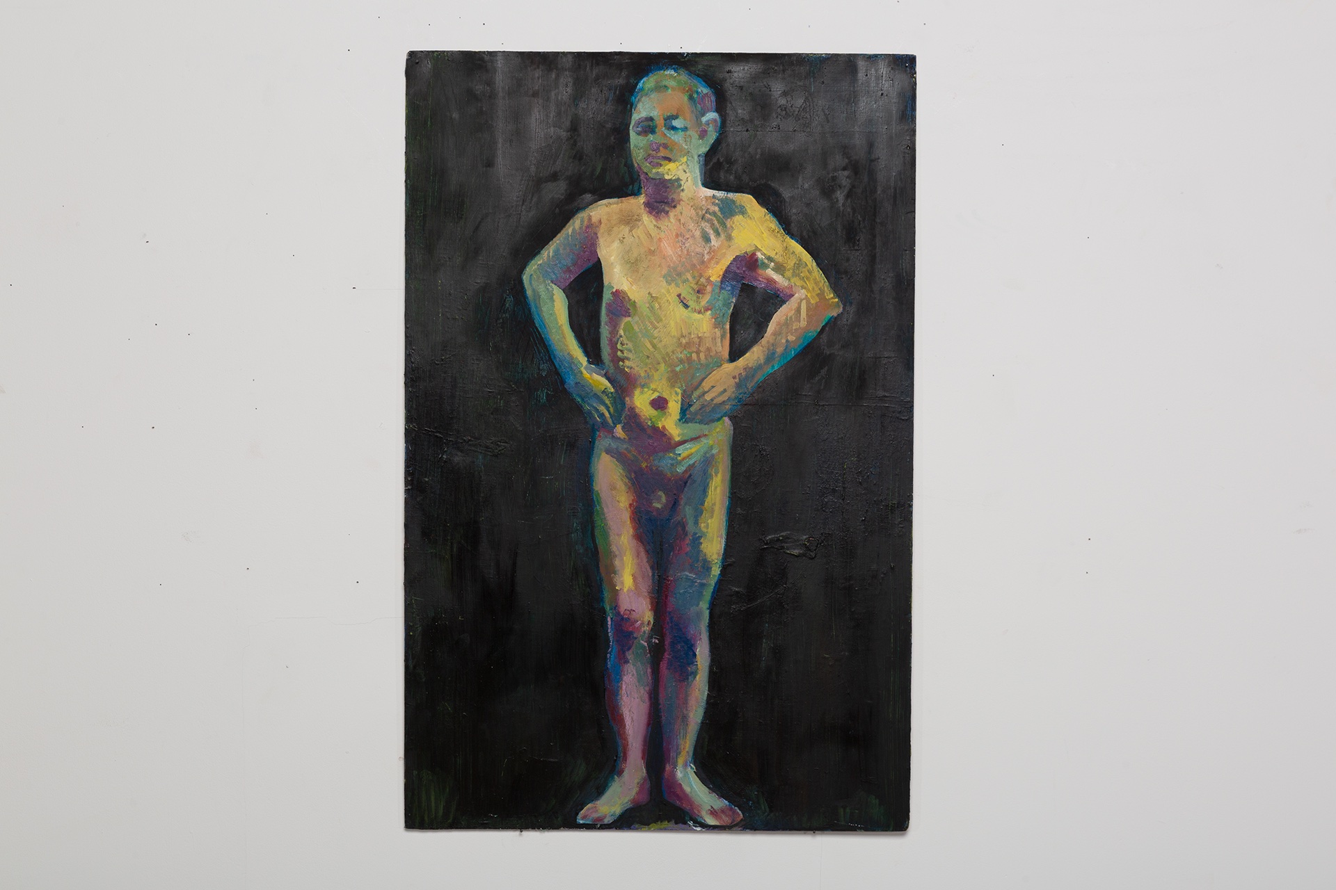 A painting of a naked person standing upright with their hands on their hips. The painting is on a white wall. The person is painted in multiple colours while the background of the painting is black.
