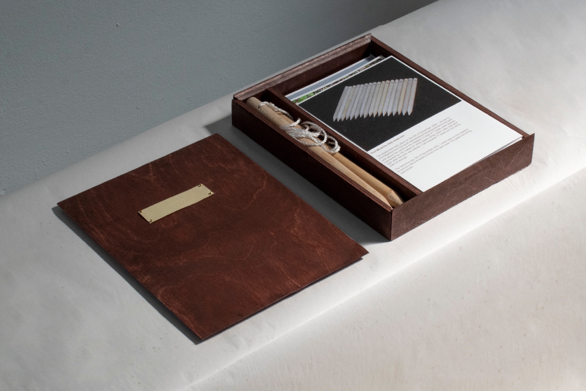 plywood box containing three accordion books, one corresponding to each field experiment and two poles with plastic string from experiment one