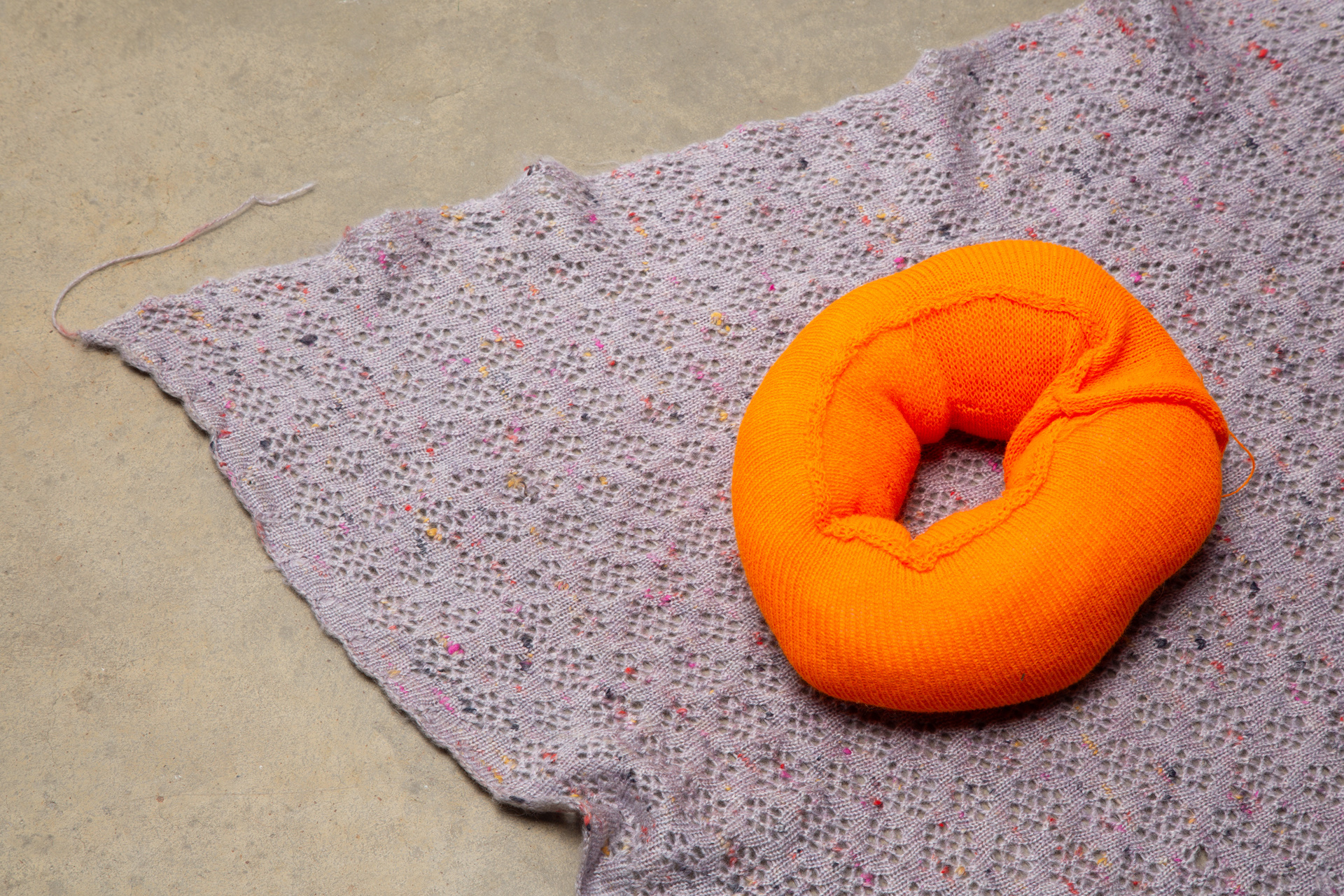 A textured purple knitted blanket with a neon orange knitted donut on top. 