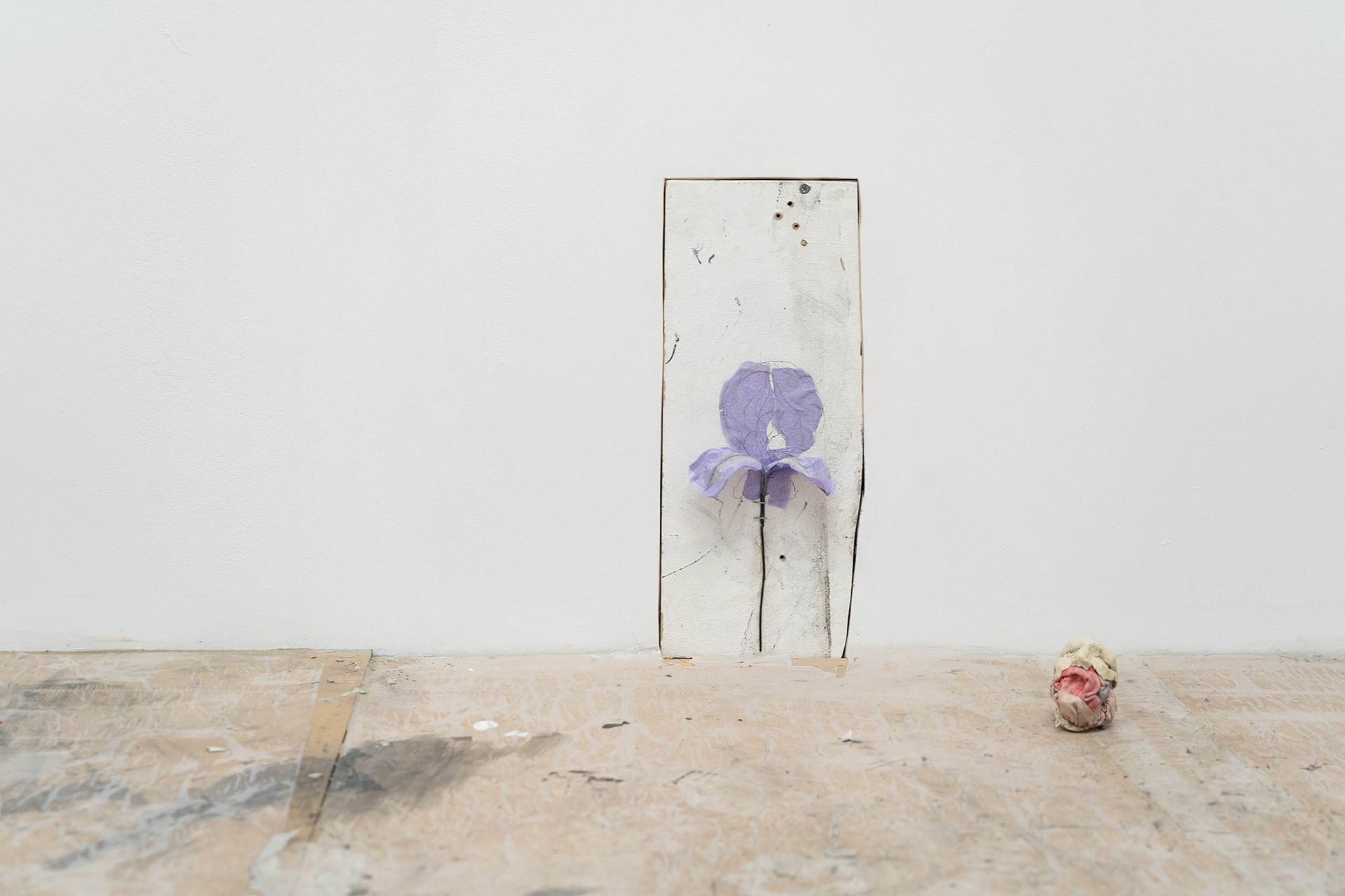 A purple paper flower mounted onto to an offcut piece of wood and set into a wall.