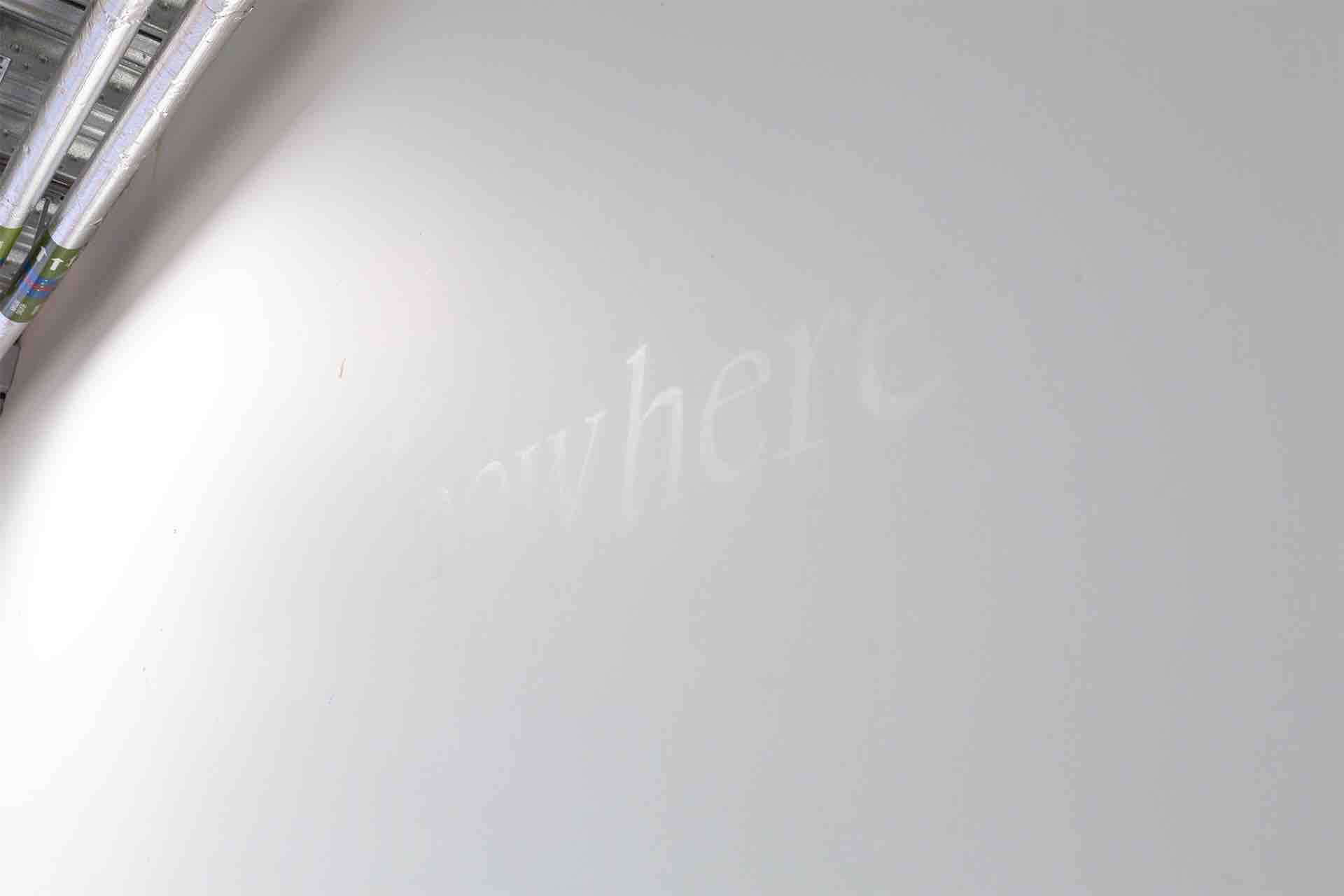 The word 'nowhere' written on a white wall in translucent wax, caught in the light.