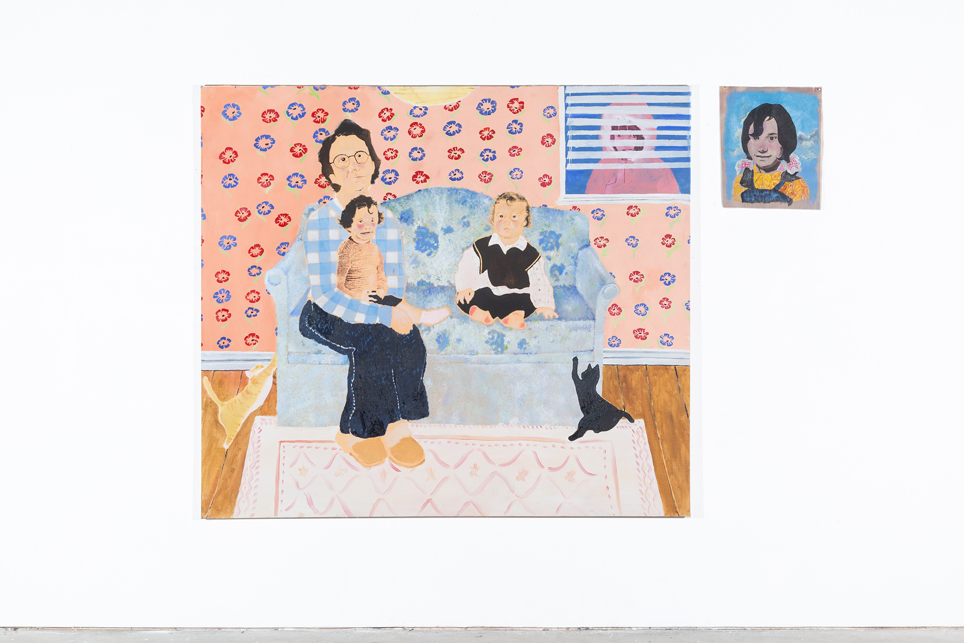 There are two paintings placed next to each other on the wall. In the first painting on the left an older woman sits on a blue floral patterned sofa with a small girl on her lap. A small boy is sat next to them on the sofa. there are two cats scratching th