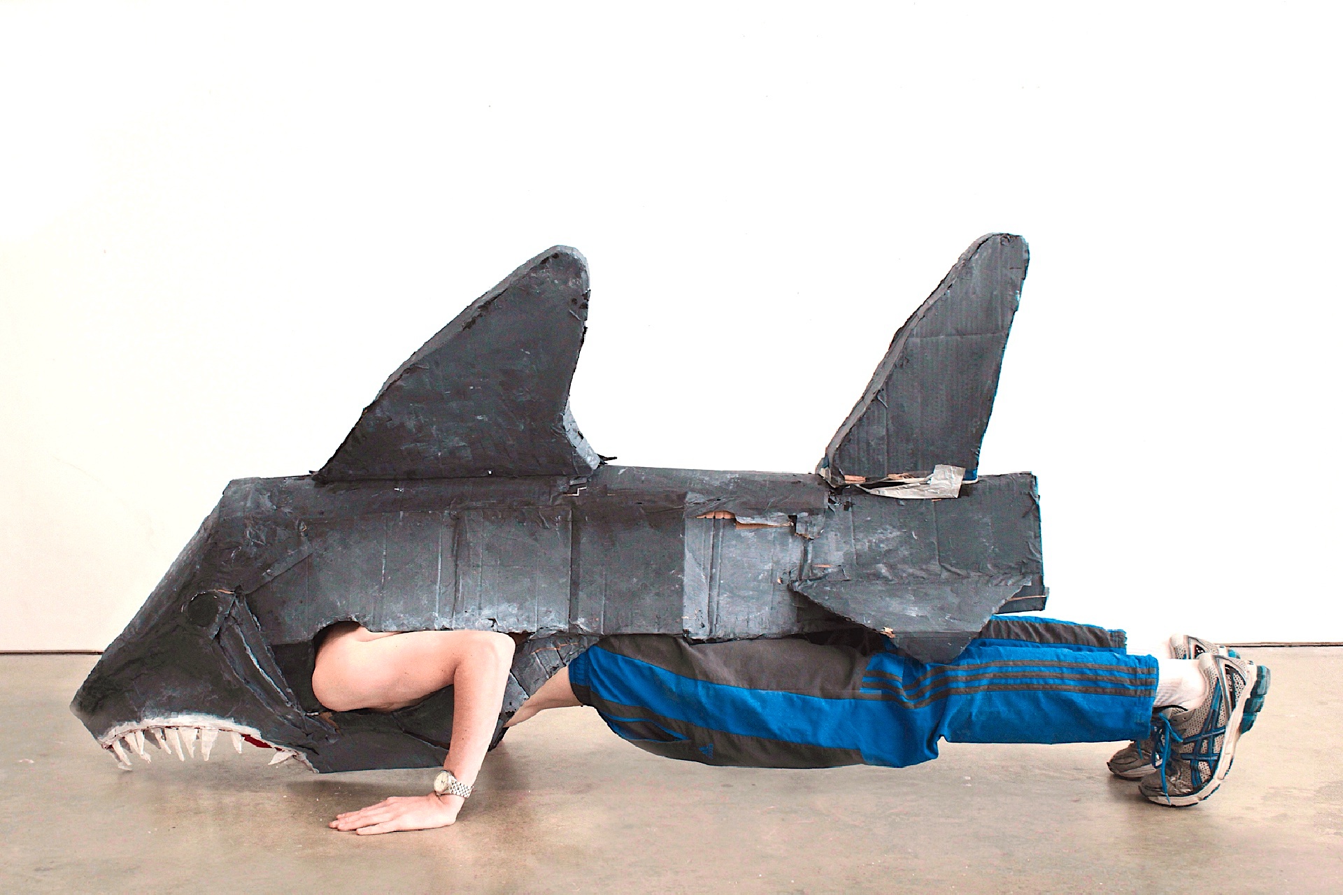 a male figure completing a press-up wearing a shark costume made out of painted cardboard and duct tape.