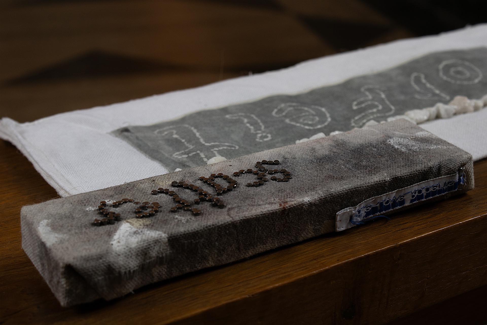 Two grey textile fabrics with writing ‘scatter’ and ‘forfeit’, resting on a chapel pew.