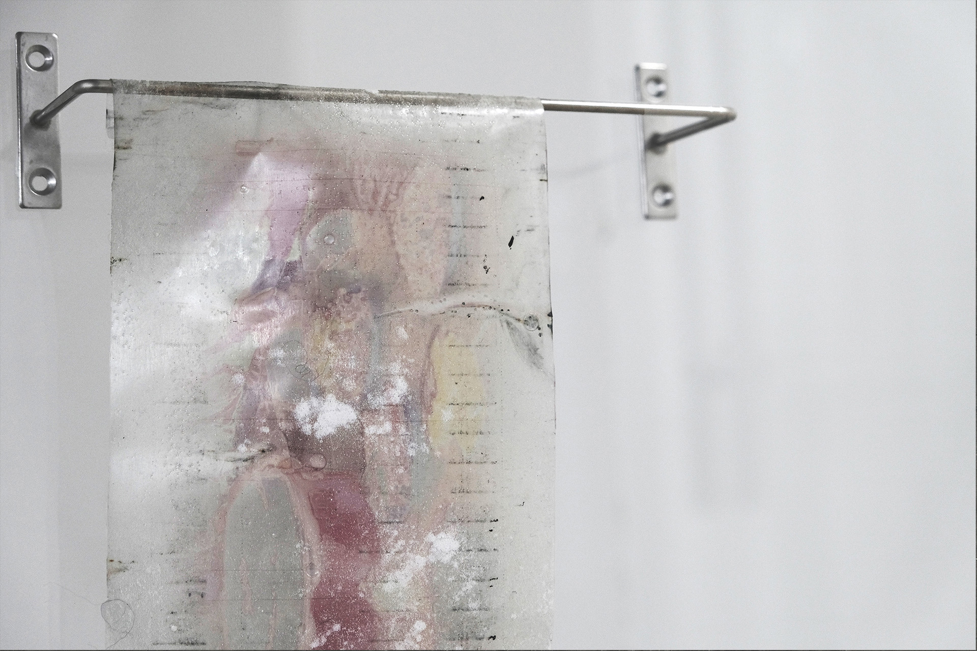 Sheet made from gelatin featuring faint, indistinct markings with flour, hanging from a metal rod attached to the wall.
