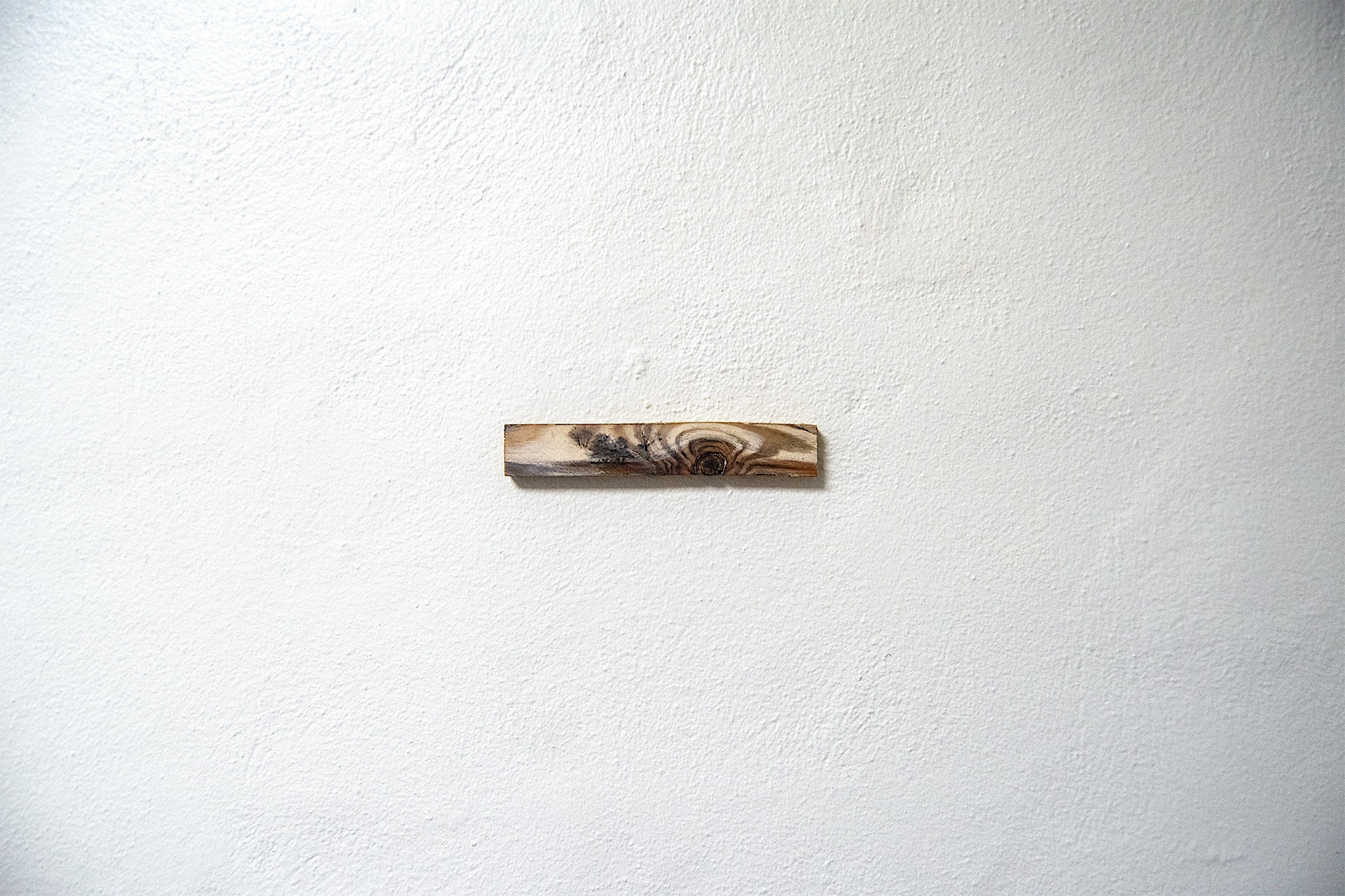 A small scale piece of wood with graphite markings making the appearance of landscapes. 