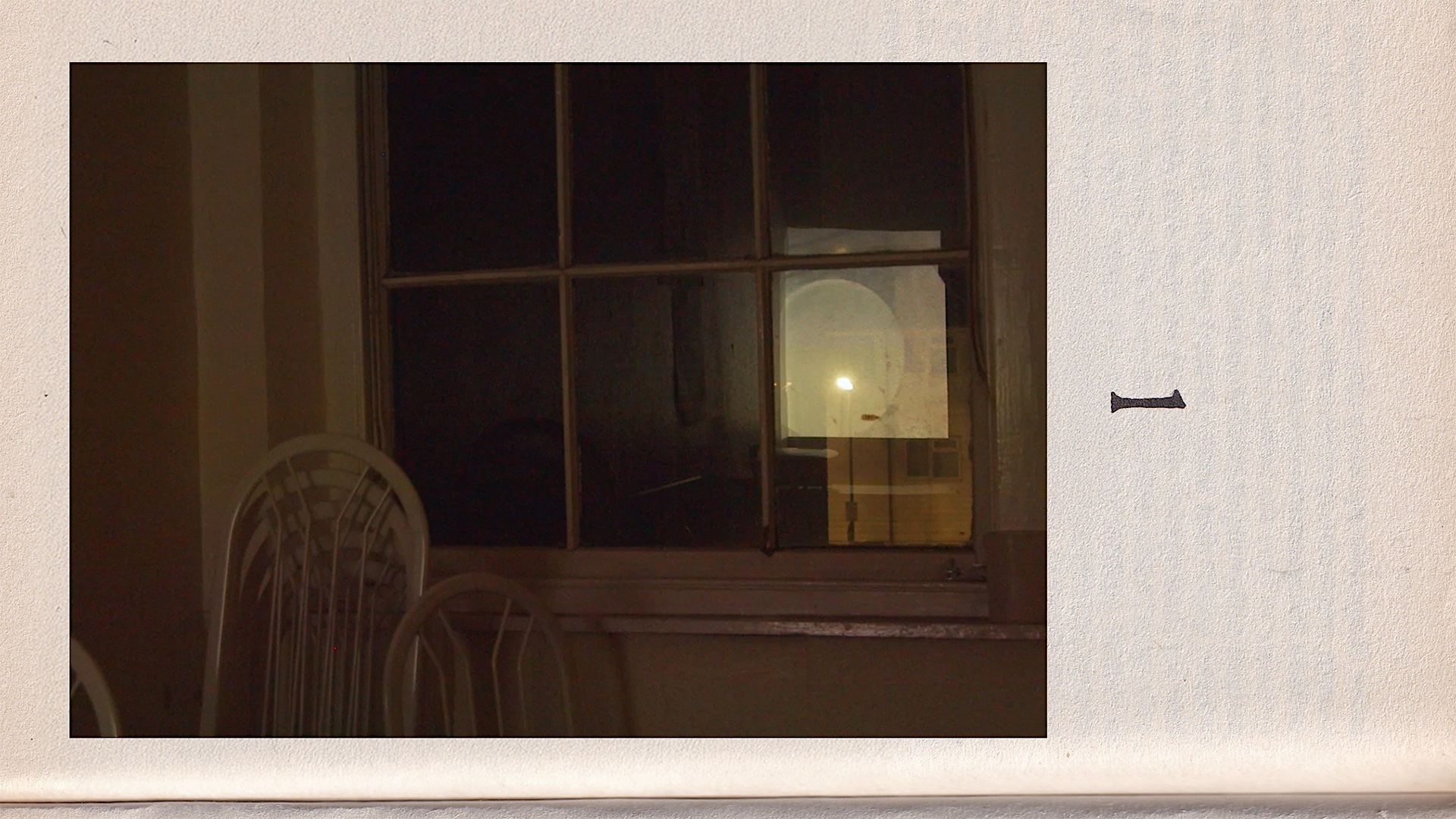 A dimly lit interior with white chairs stacked in front of a window. A circular form is reflected in the glass. The image is embedded in a textured paper background with a printed numeral “1” beside it, suggesting a book page layout.
