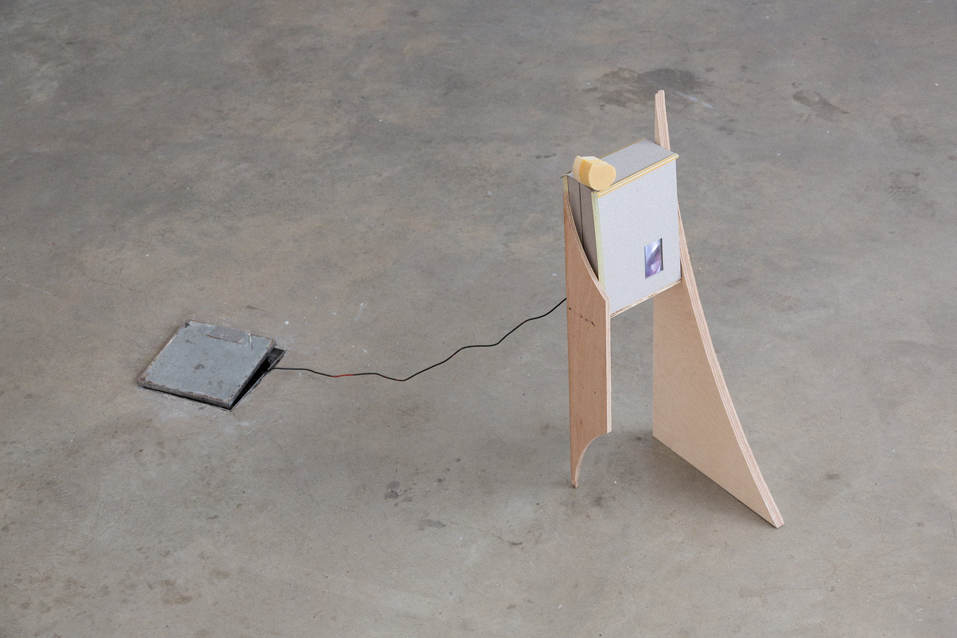 A sculpture of a greyboard box containing a screen balanced on a timber frame