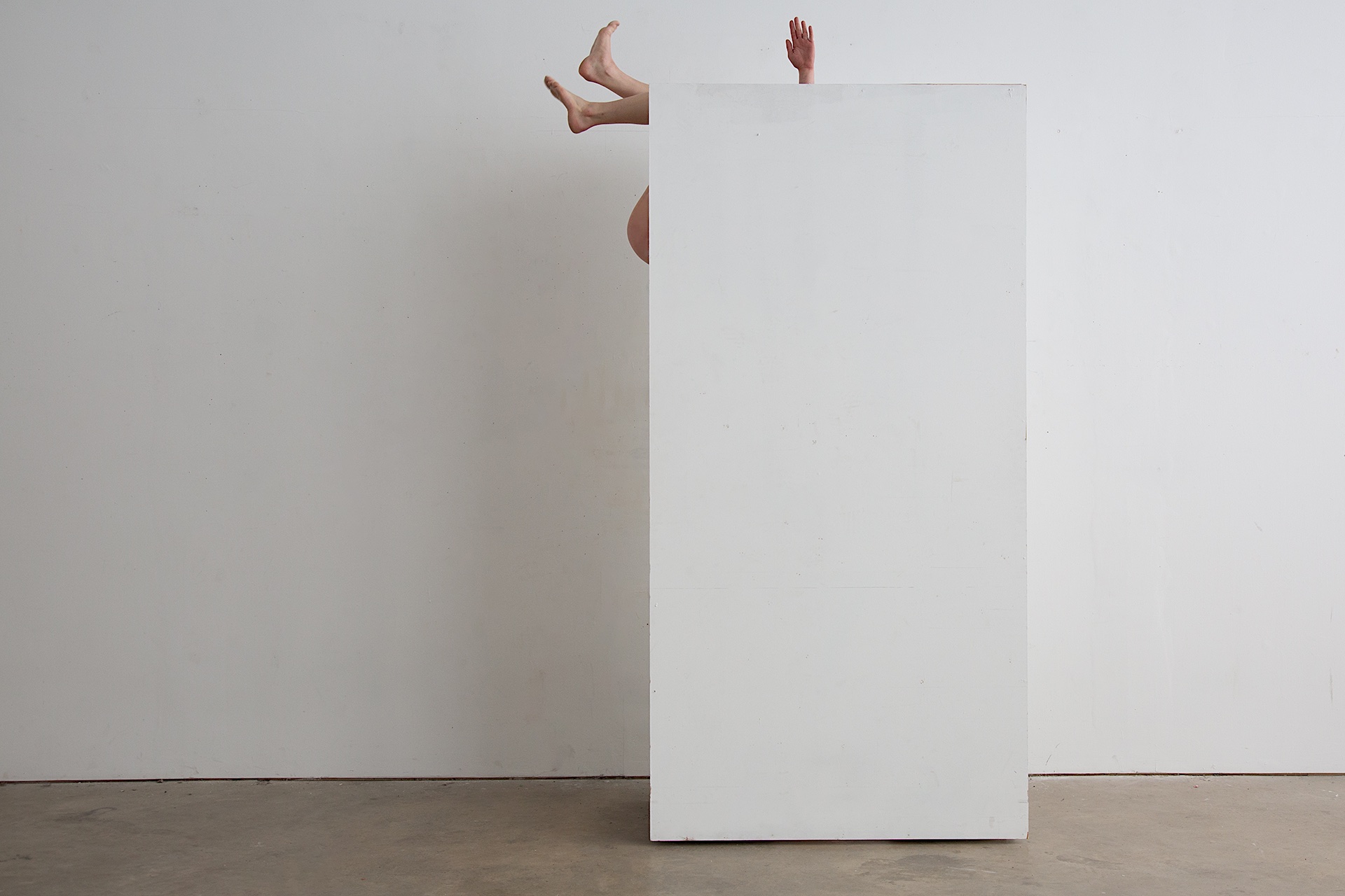 Performance still with legs and arms of a figure emerging from behind a wall