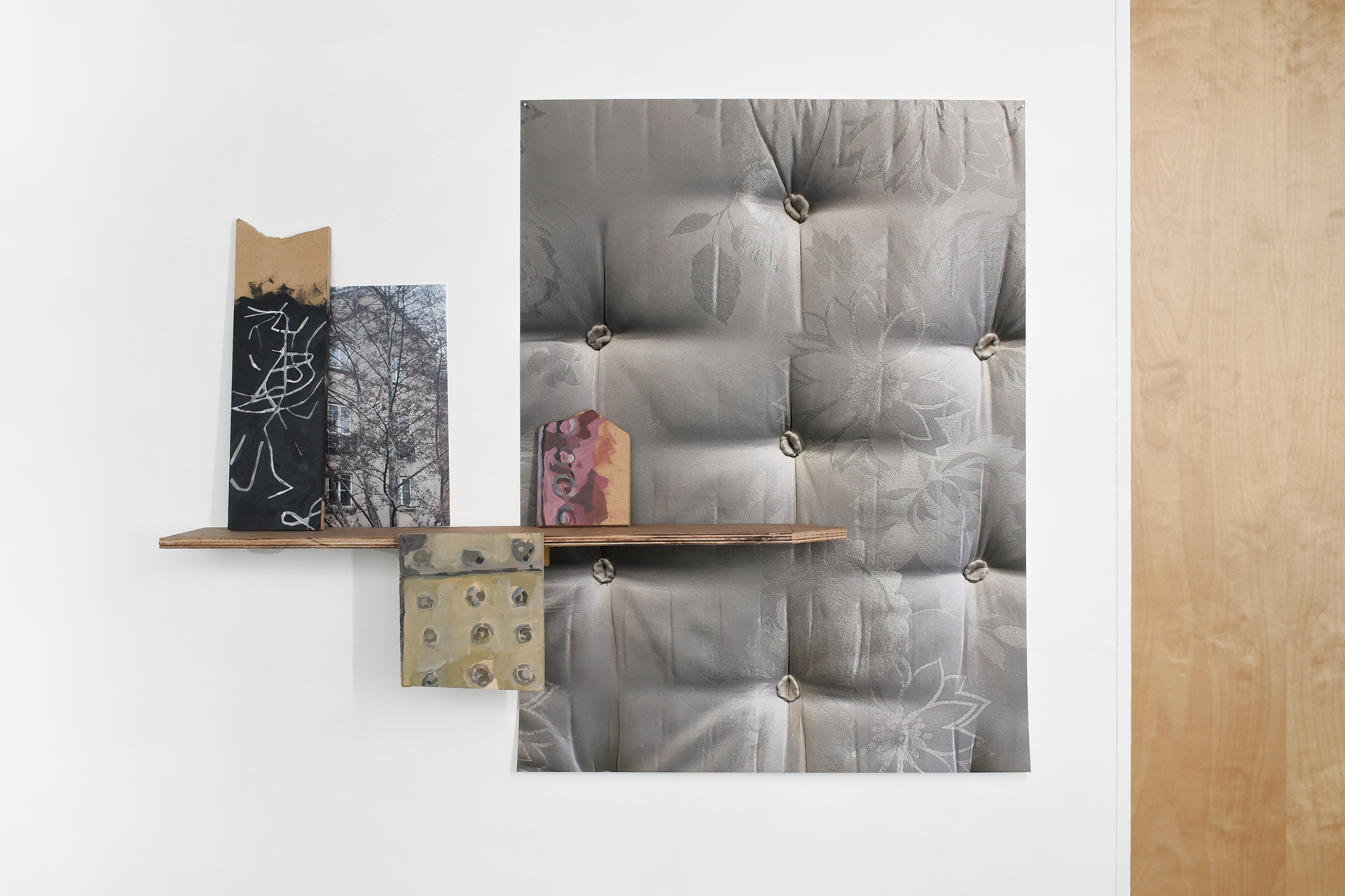 A selection of printed photographs arranged with a wooden shelf and two paintings on a wall. The largest image is of a mattress and the smaller image of a house and tree. The paintings are of the road.