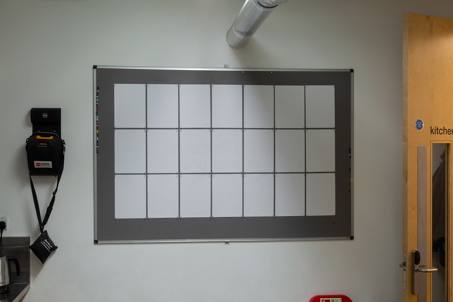 Photograph depicting a large, felt noticboard upon which 21 sheets of A4 paper are pinned. Across said sheets the phrase 