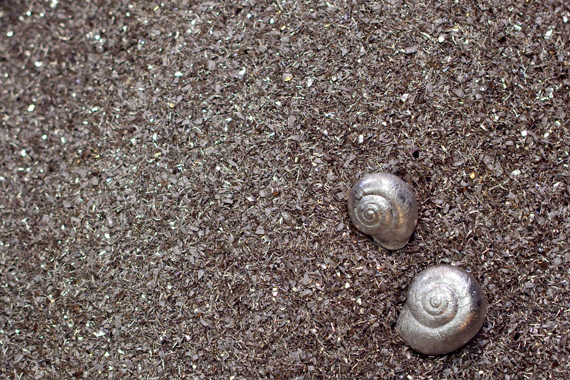 Snail shells cast from bell bronze, laying on a bed of silver metal shavings.