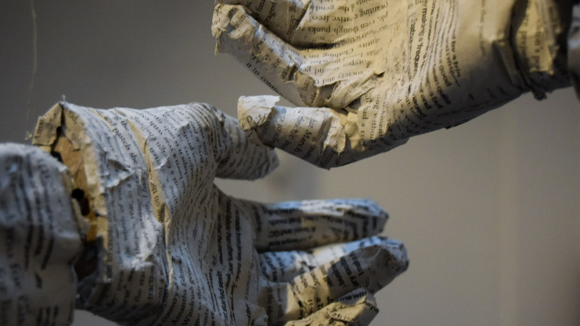 A close-up photo of two hands (made of paper and covered in text) gently touching. Stranger : Won’t you look me in the eye? (kinetic sculpture) 