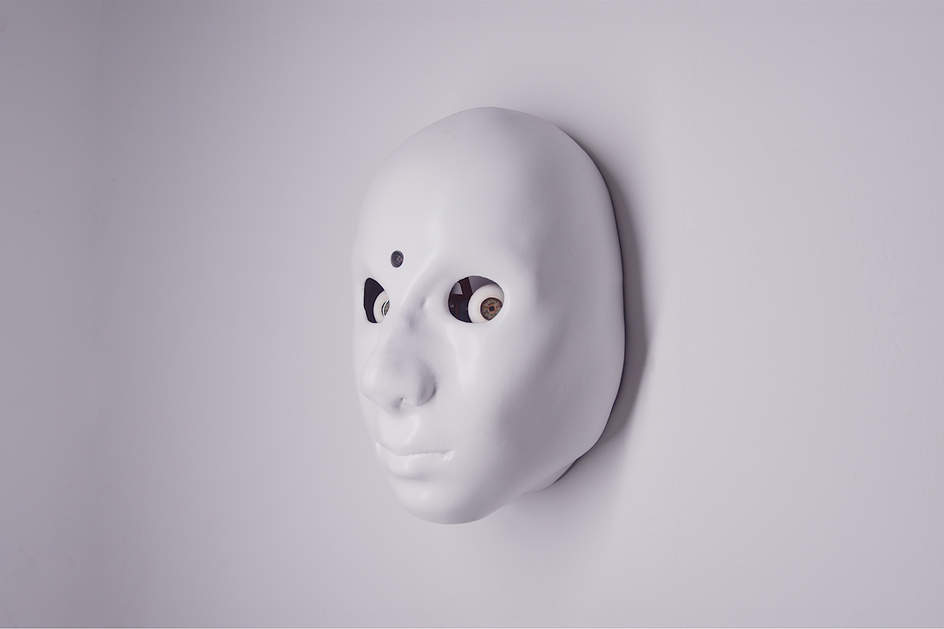 A pure white face protrudes from the wall. Their eyes reflect the light as they stare straight at you. 