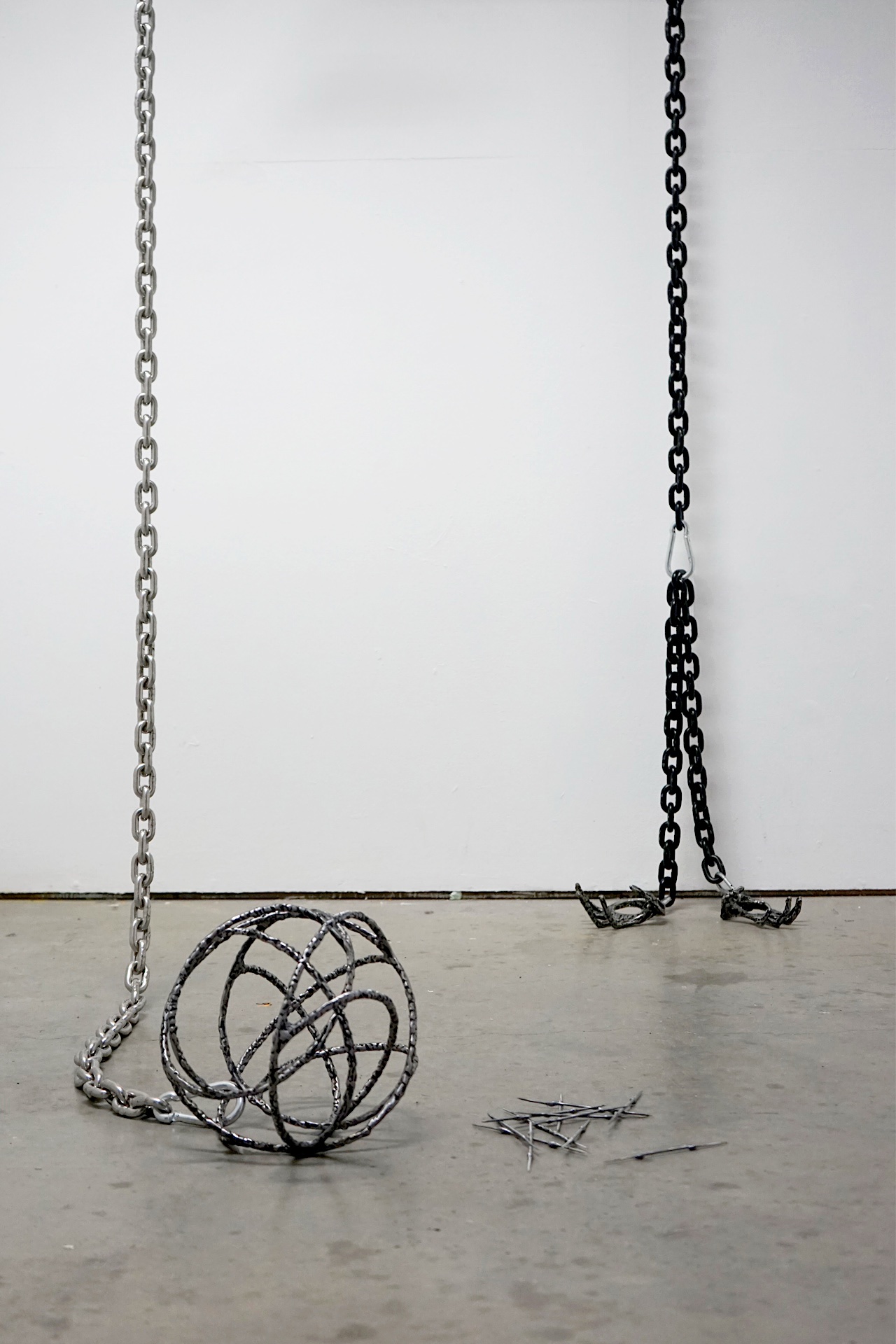 A sheet of steel marked with the residue from newspaper, spray paint and tar is suspended from the ceiling by blue straps. The sculpture features two holes on either side of the metal, wrapped with blue climbing rope that spills onto the floor, coiling nea