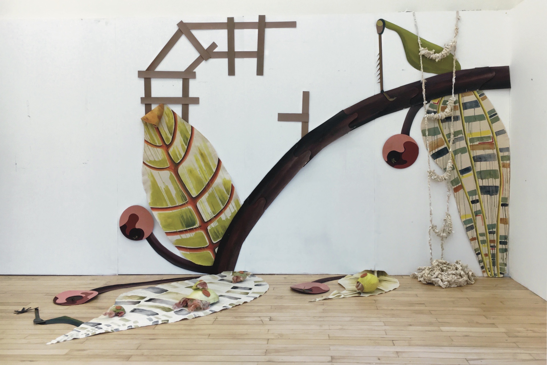 An installation that is 9 x 12 x 6 ft made of acrylic paint, canvas, cotton, stuffing, and greyboard. Part of the installation is hung on the wall and part is on the floor. It has large leaves painted in colorful patterns. There are grasshopper legs, a ste