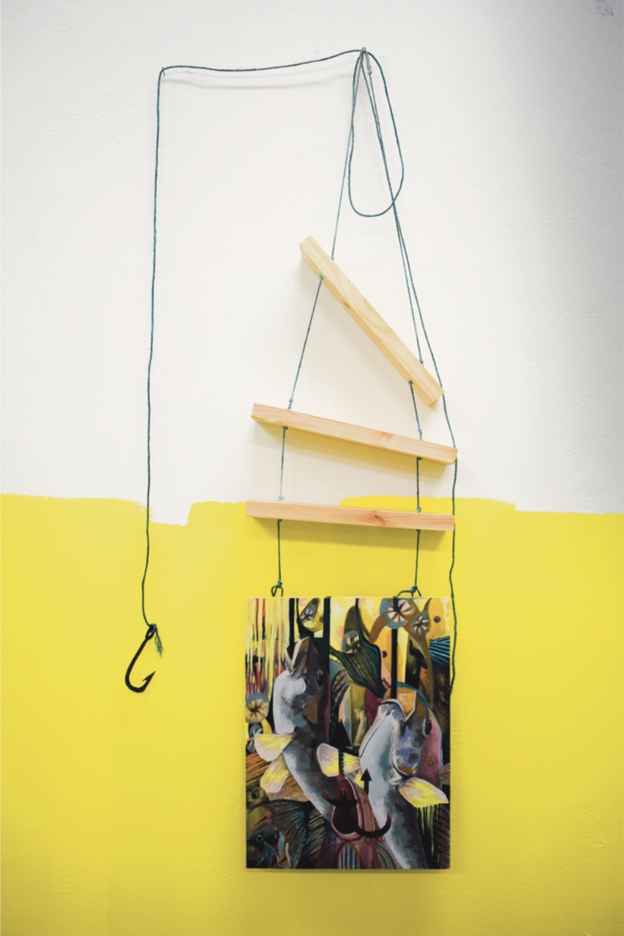 A painting of fish that have been caught on fishing hooks. Attached at the top of the painting is a ladder made of rope and wood. There is a fish hook that is hung using the same rope as the ladder at the side of the painting. The piece is hung on a wall t