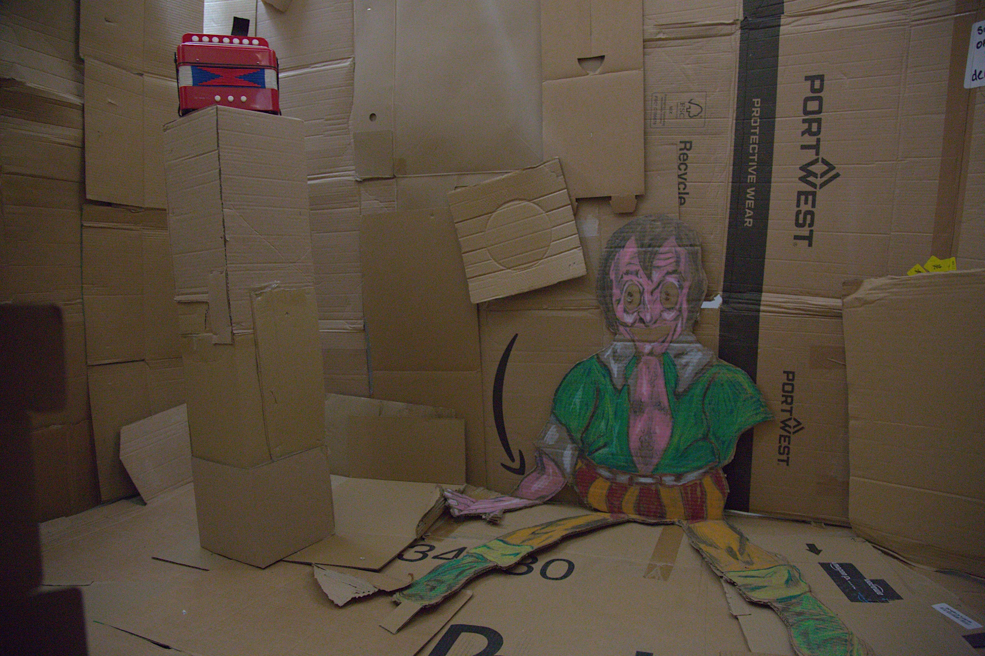 A cardboard creature and a children's acordian in a cardboard room accused by a cardboard tunnel 