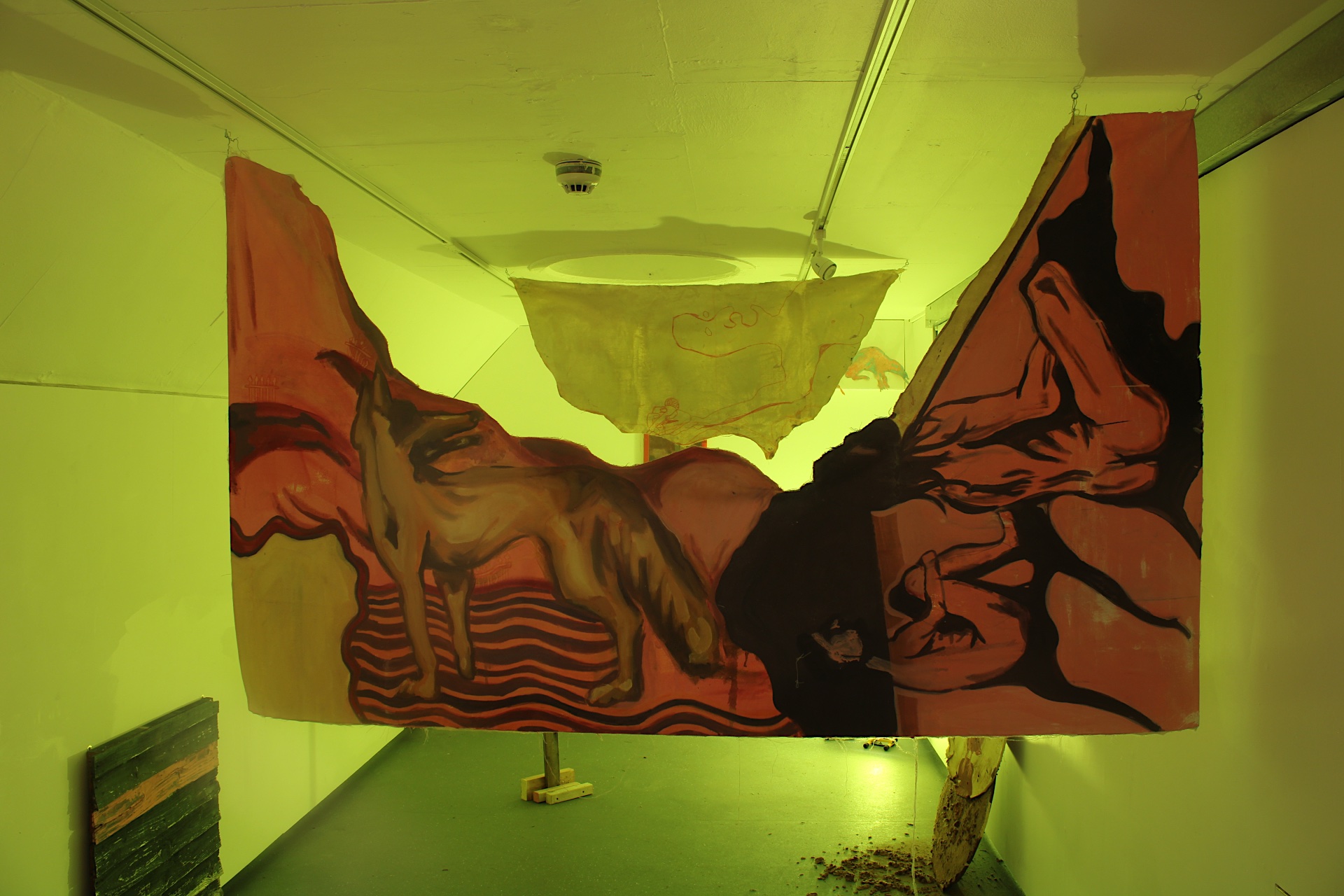 An installation with bright yellow lighting. A painting cut into two hangs at different points in a long, thin room.