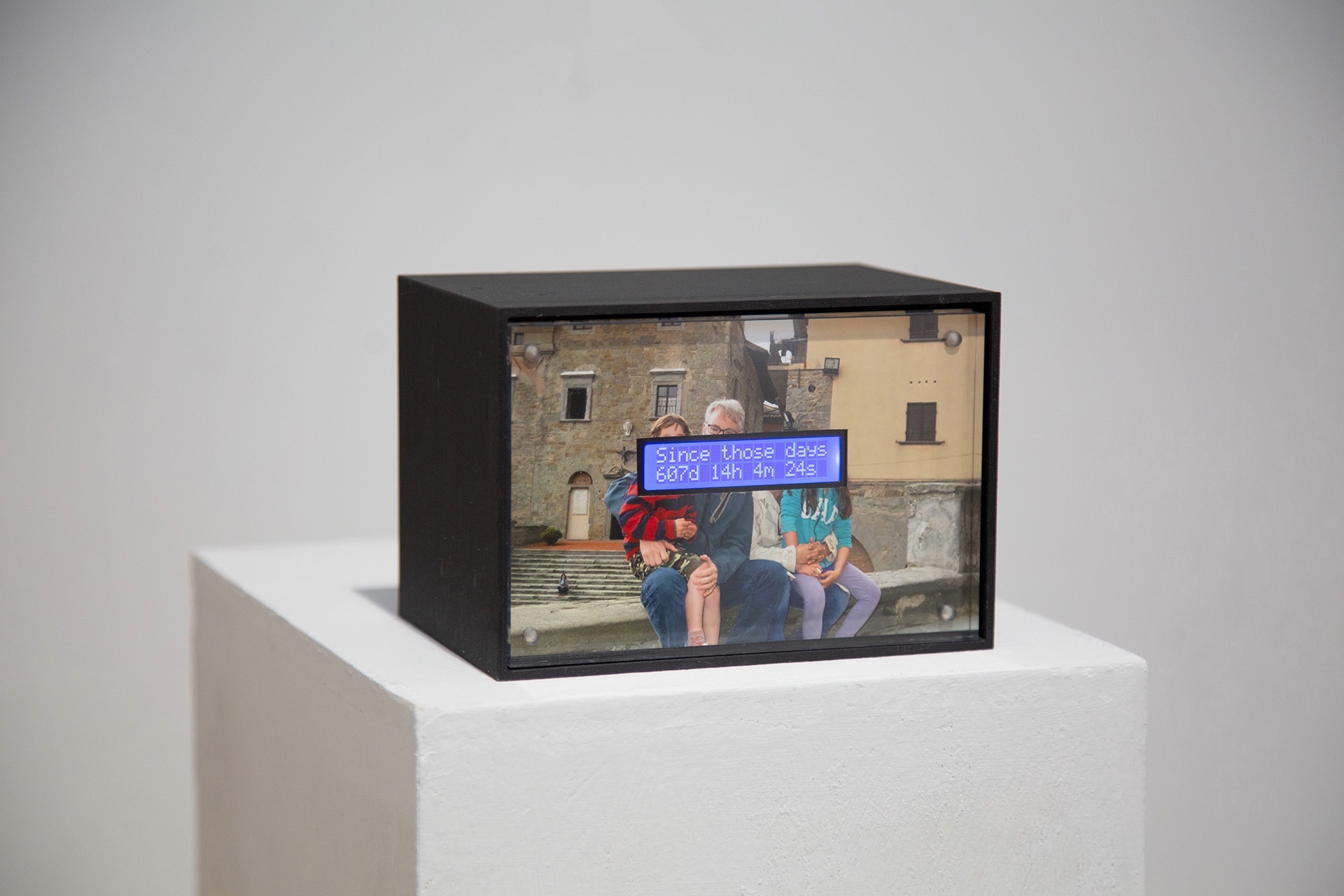 Boxed display on pedestal shows family photo with digital timer reading “Since those days.”