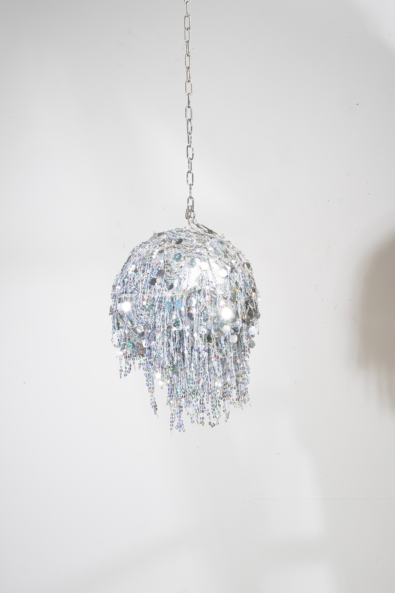 Silver, sparkly disco ball hanging from a chain.