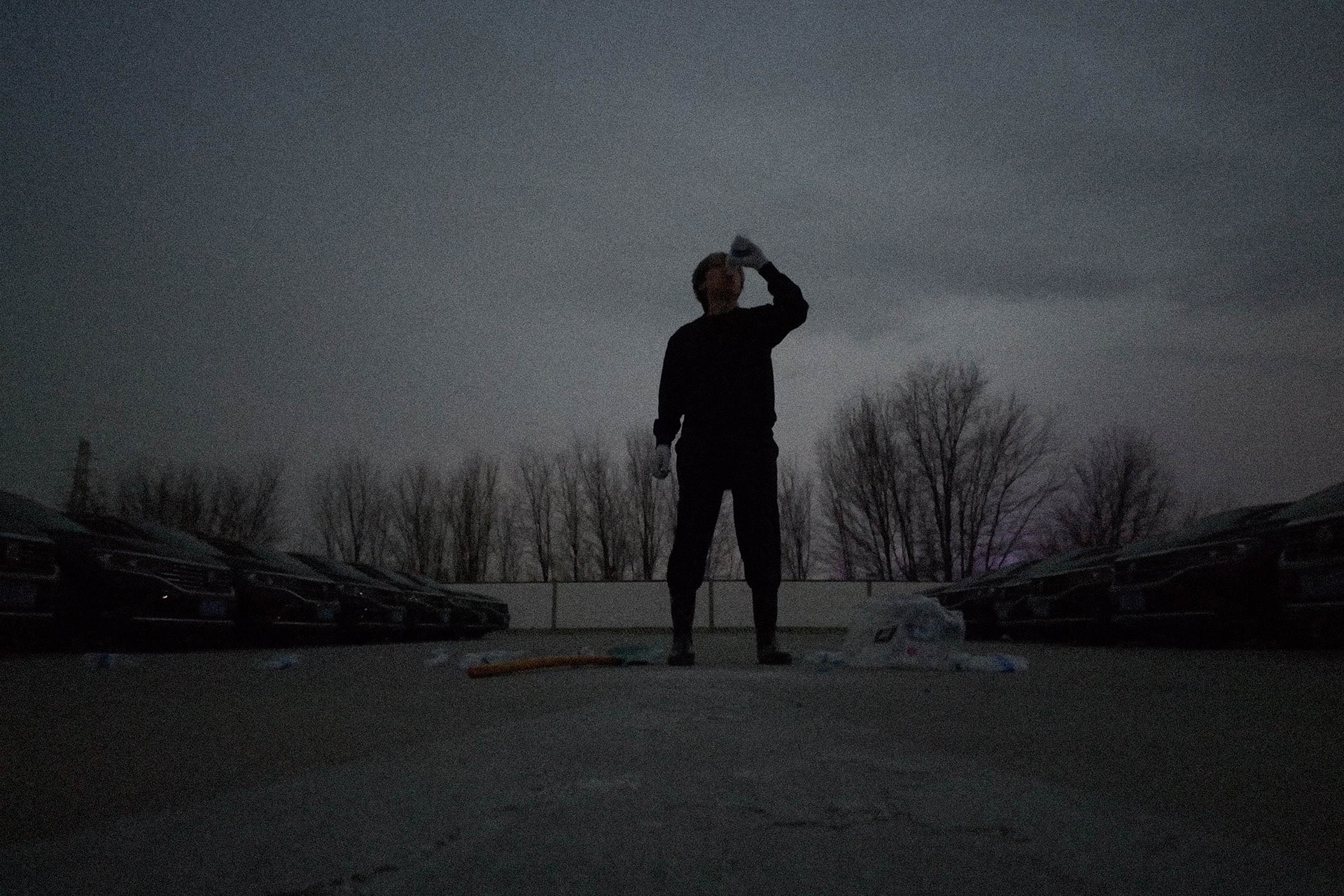 The scene is slightly dark. The artist stands in the center of the frame, holding up a bottle of mineral water in her right hand and drinking from it. At the artist’s feet are many mineral water bottles and a shovel, and on the left and right sides are two