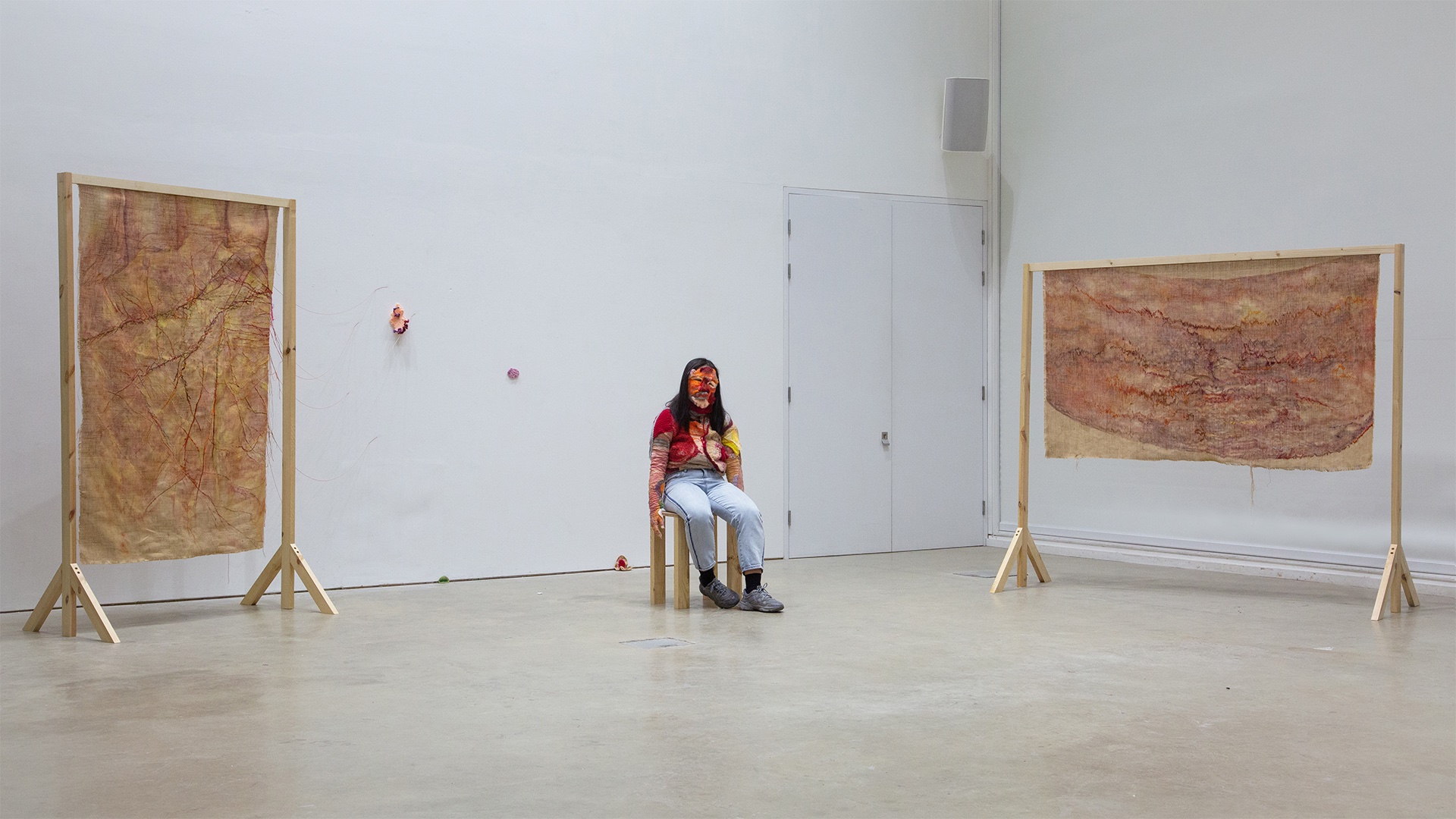 Female wearing hand-knitted and crocheted skin sitting with two hung oil on hessian fabric with hand embroidery