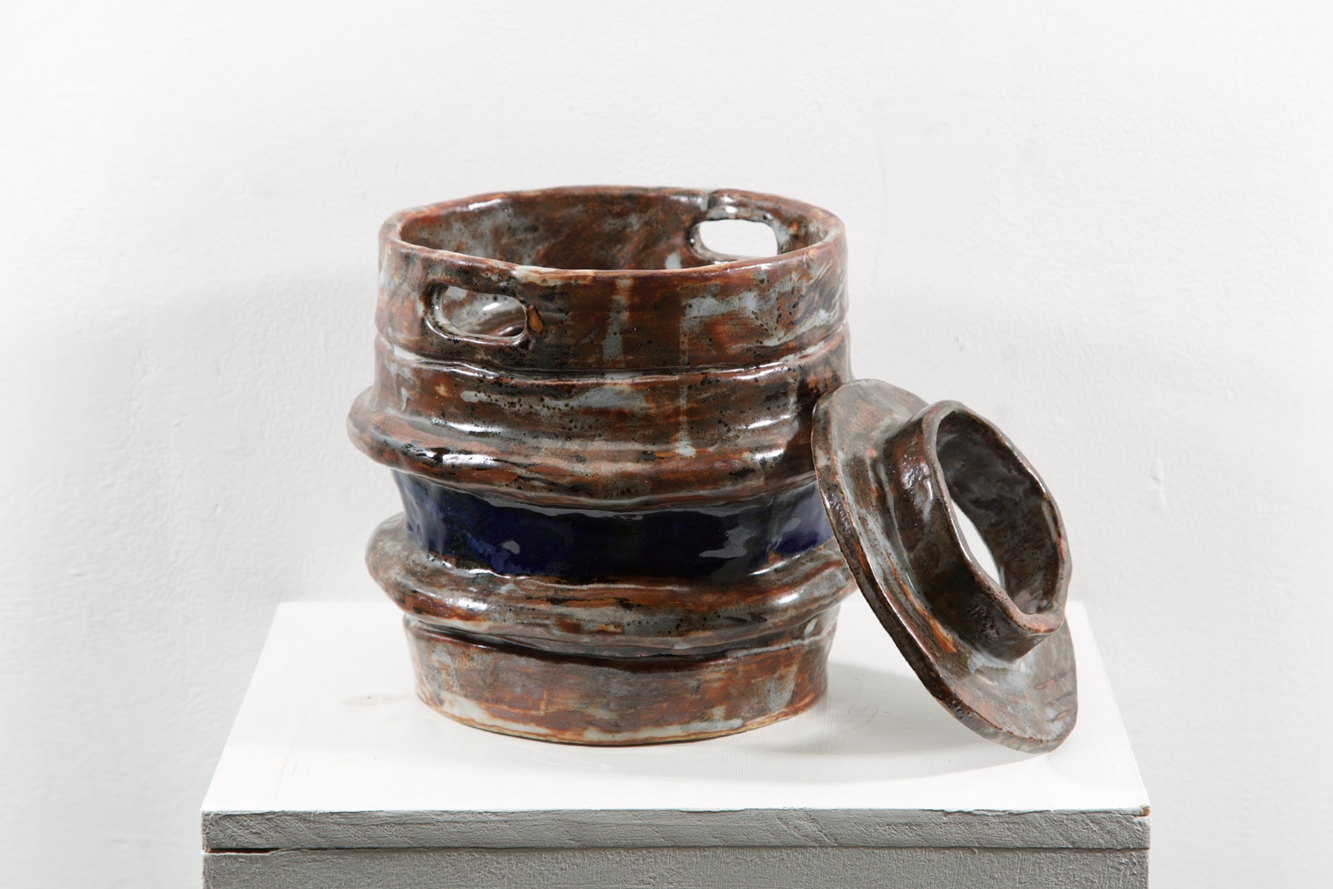 A rusted beer keg with a blue stripe made from ceramic on a white plinth.