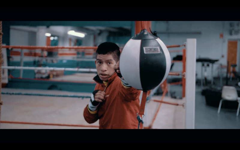 A still from a film by Eli Zuzovsky showing a young man in a boxing ring hitting a ball.