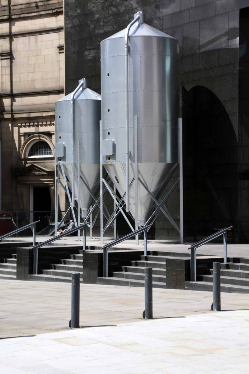 Two small steel silos side by side in an industrial environment.